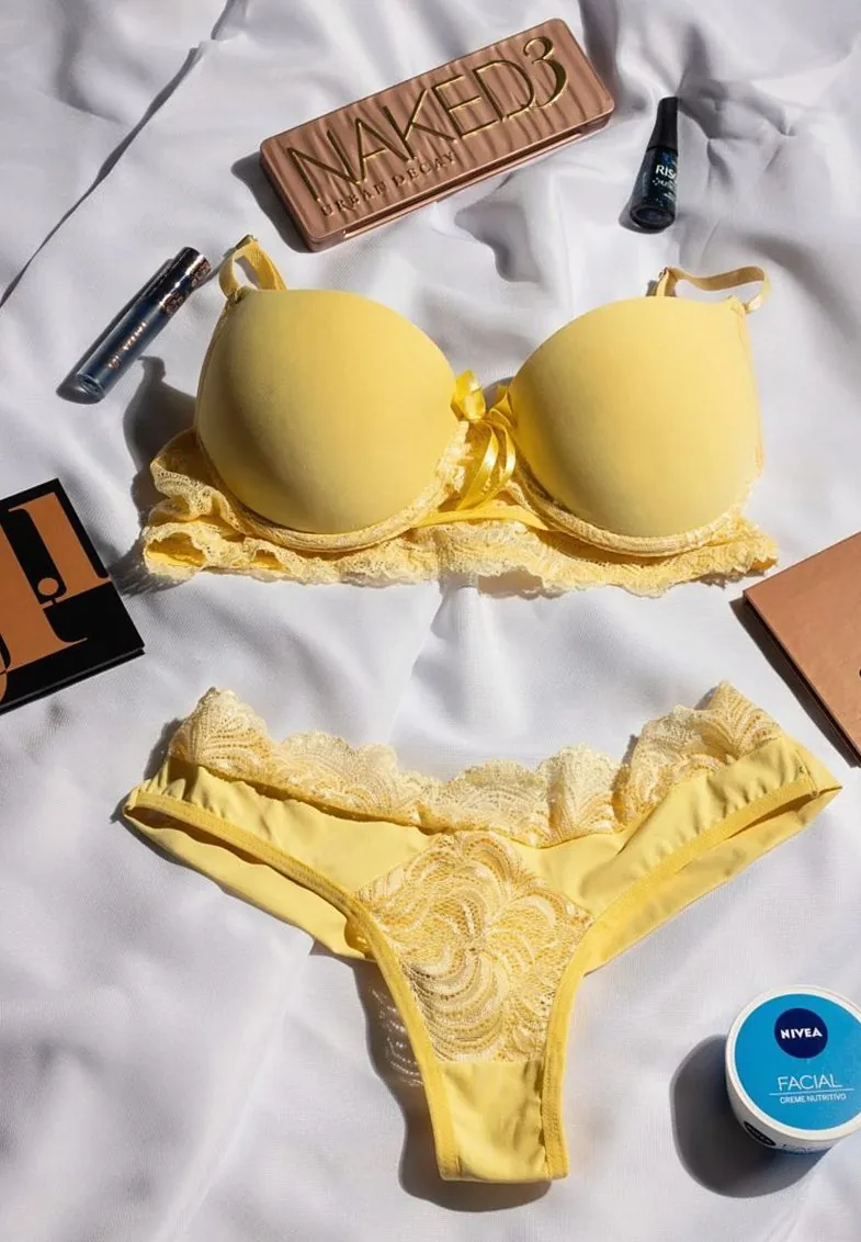Flat lay of yellow lingerie set with beauty products on a white background.