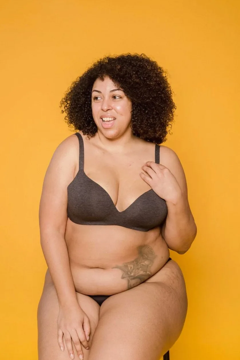 Positive plus size African American female model with tattoo wearing black lingerie looking away while sitting on yellow